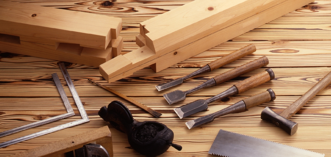 Traditional woodworking chisels, a hammer, and timber joints on a wooden workbench